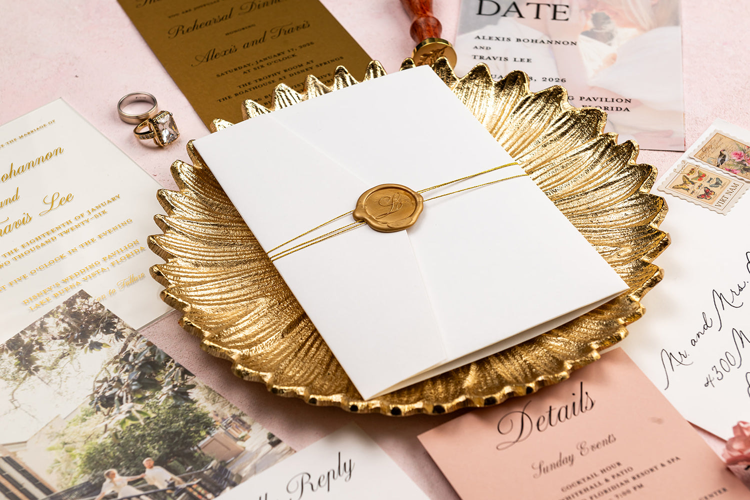 White invitation card with gold seal on a decorative gold plate surrounded by other invitations and stationery items.