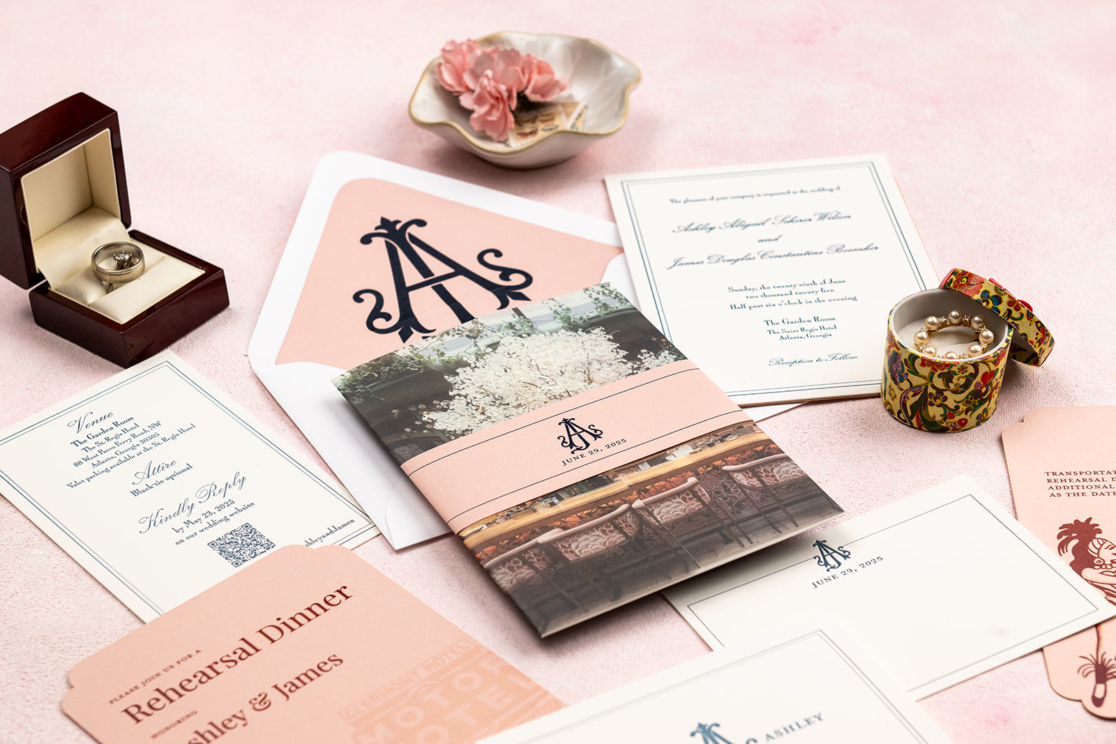 Letterpress wedding invitation set with monogram, ring, and flowers on a pink surface. 