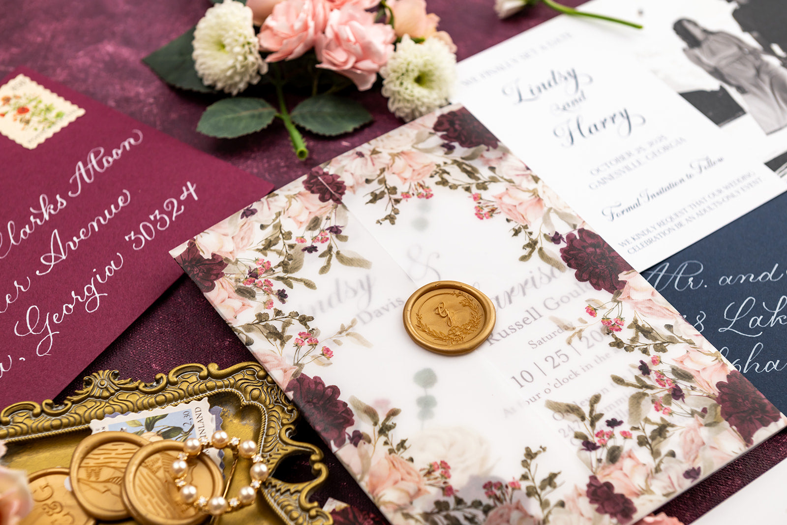 Wedding invitation set with floral vellum wrap design, wax seals, and decorative elements on a dark surface.