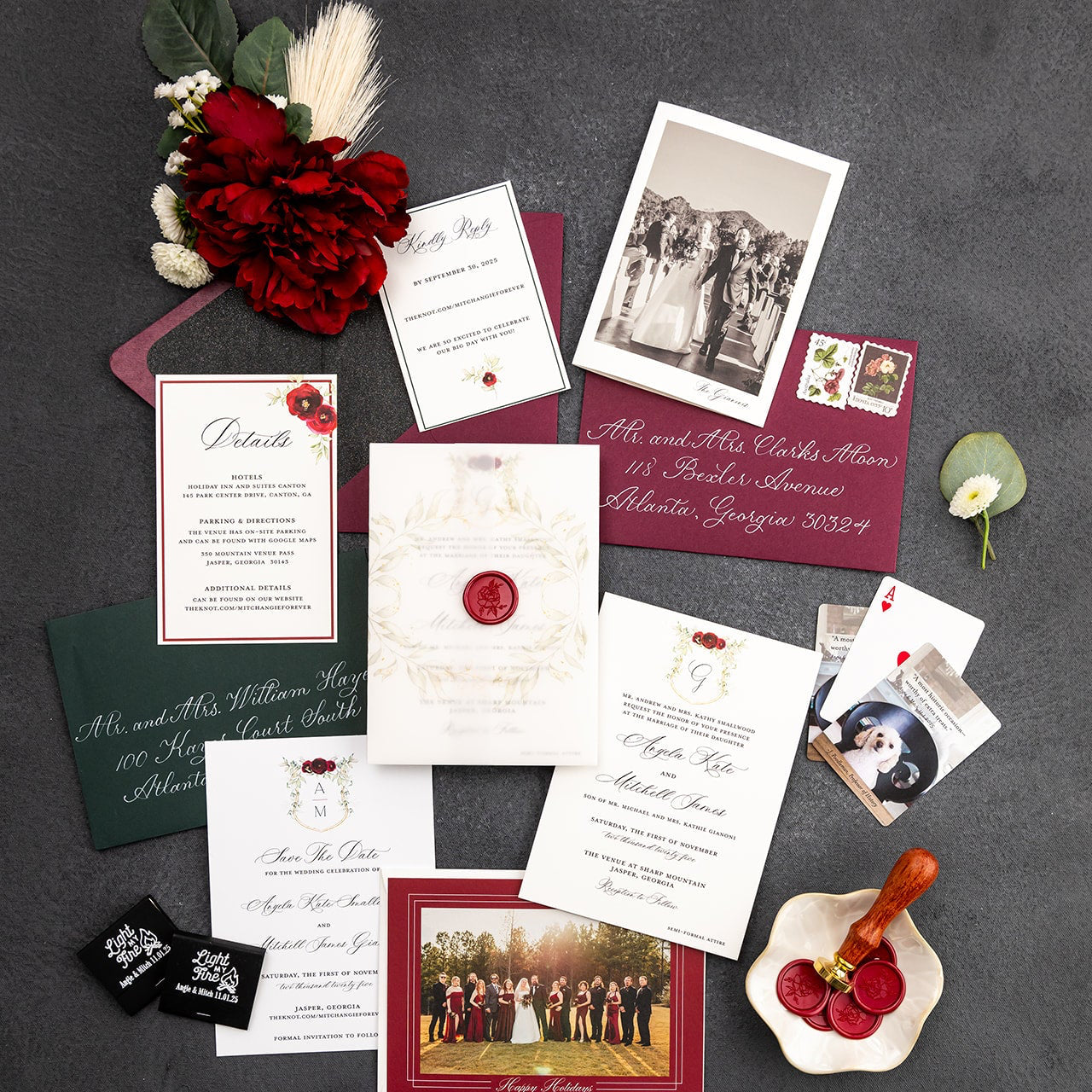 Collection of fall or winter wedding invitations and stationery items on a dark surface with flowers and a photo album.